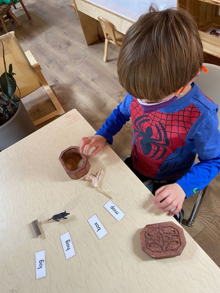 A child busy matching objects with CVC words. This activity helps in the development of reading and writing skills. Miniature objects are a point of interest.